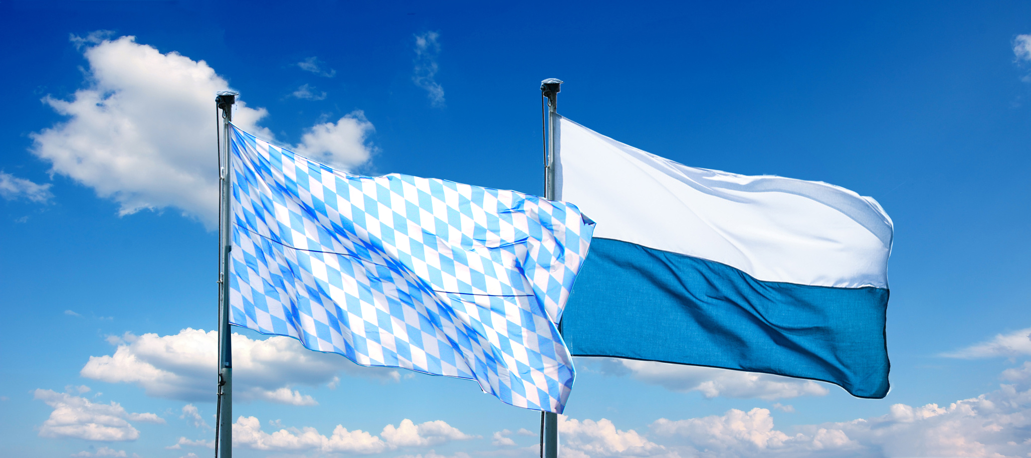 Die Rautenflagge (links) und die Streifenflagge (rechts) vor blauem Himmel mit Wolken.