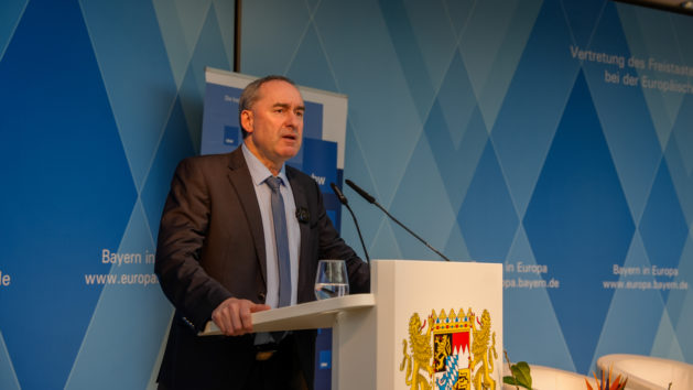 Minister Aiwanger h&auml;lt seine Begr&uuml;&szlig;ung am Stehpult, auf dem das Staatswappen zu sehen ist. Im Hintergrund sieht man die Rautenwand der Vertretung.