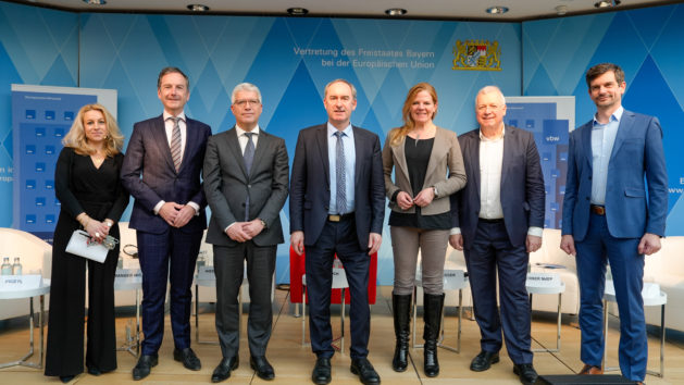 Die sieben Sprecher stehen zum abschlie&szlig;enden Gruppenbild nebeneinander auf der B&uuml;hne. Im Hintergrund sieht man die blaue Rautenwand der Bayerischen Vertretung.